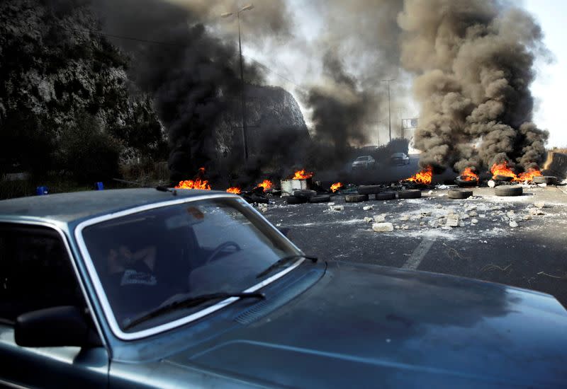 FILE PHOTO: A man sleeps in a car next to burning tires barricading the highway during ongoing anti-government protests at Nahr El Kalb