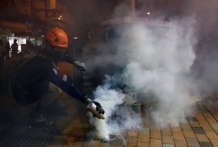 An anti-extradition bill protester tries to extinguish a tear gas canister after the police fired tear gas to disperse the demonstration at Sham Shui Po, in Hong Kong