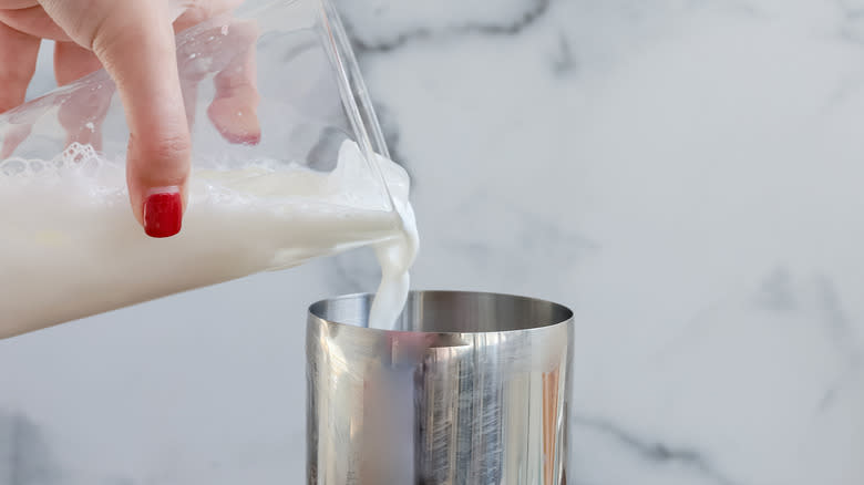 hand pouring mixture into cocktail shaker