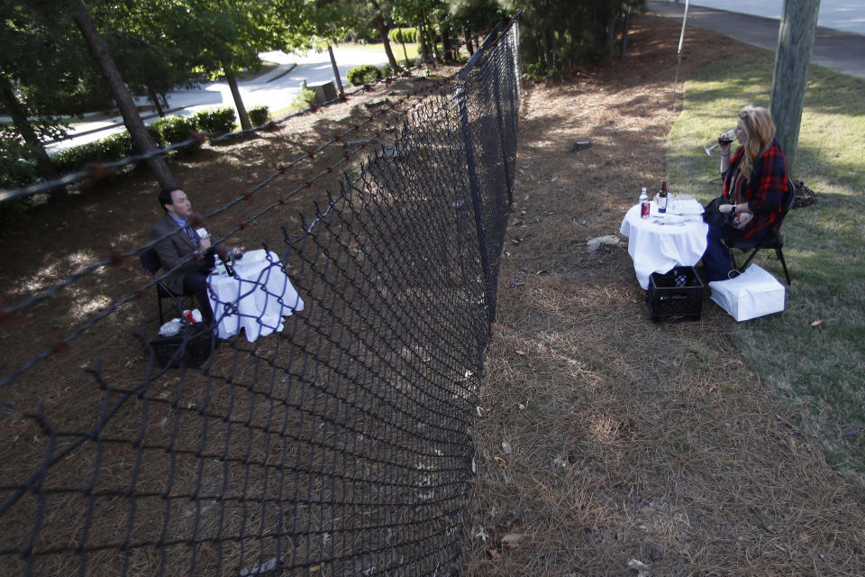 FILE - In this April 30, 2020 file photo, Justin and Crystal Craft enjoy their weekly dinner date on opposite sides of a fence surrounding the Park Springs senior community, where Justin runs the food and beverage department, in Stone Mountain, Ga. Workers who agreed to live at a Georgia nursing home to keep its residents safe from the coronavirus will embrace their loved ones for the first time in more than two months on Saturday, June 13 as the home lifts a shelter-in-place restriction on its staff. (AP Photo/John Bazemore, File)