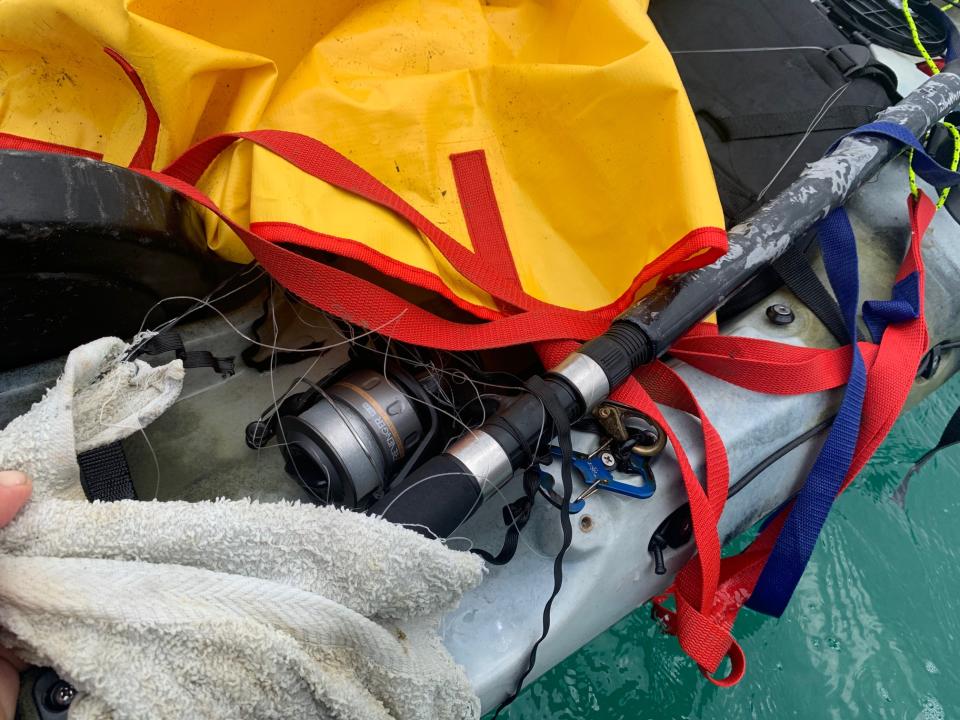 An empty fishing kayak is seen. Inside is a fishing rod with a tangled line.