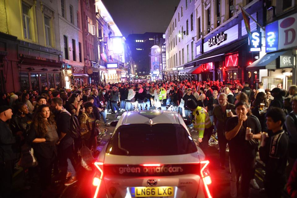 TOPSHOT - A car tries to drive along a street filled with revellers drinking in the Soho area of London on July 4, 2020, after the police re-opened the road at 2300 as restrictions are further eased during the novel coronavirus COVID-19 pandemic. - Pubs in England reopen on Saturday for the first time since late March, bringing cheer to drinkers and the industry but fears of public disorder and fresh coronavirus cases. (Photo by JUSTIN TALLIS / AFP) (Photo by JUSTIN TALLIS/AFP via Getty Images)