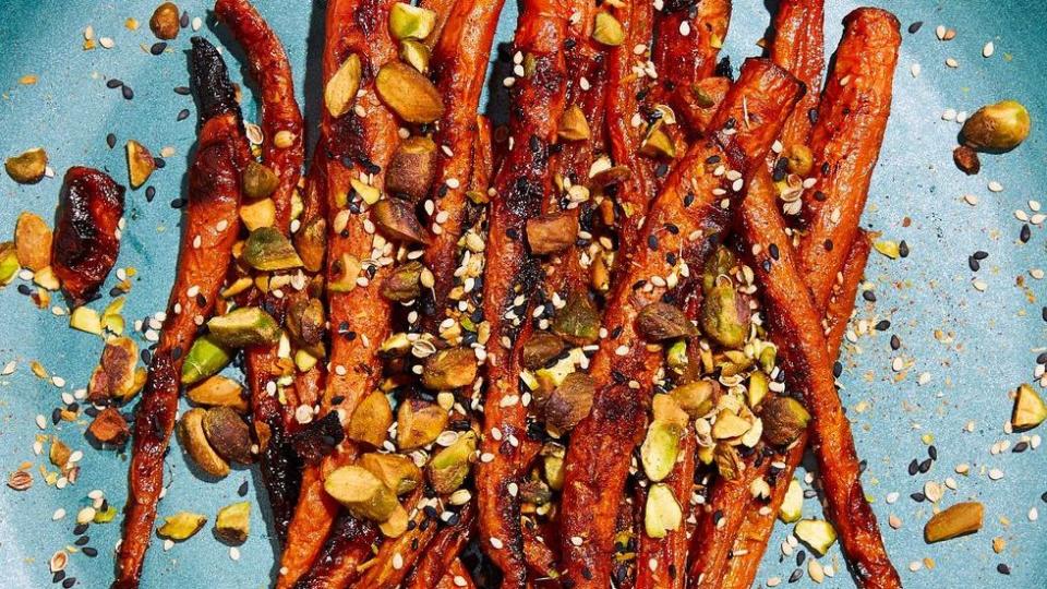 miso roasted carrots topped with pistachios and black and white sesame seeds on a teal plate