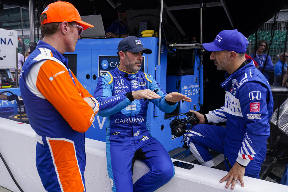 Jimmie Johnson, center, talks with Scott Dixon, of New Zealand, left and Tony Kanaan, of Brazil, during practice for the IndyCar auto race at Indianapolis Motor Speedway in Indianapolis, Thursday, May 19, 2022. (AP Photo/Michael Conroy)