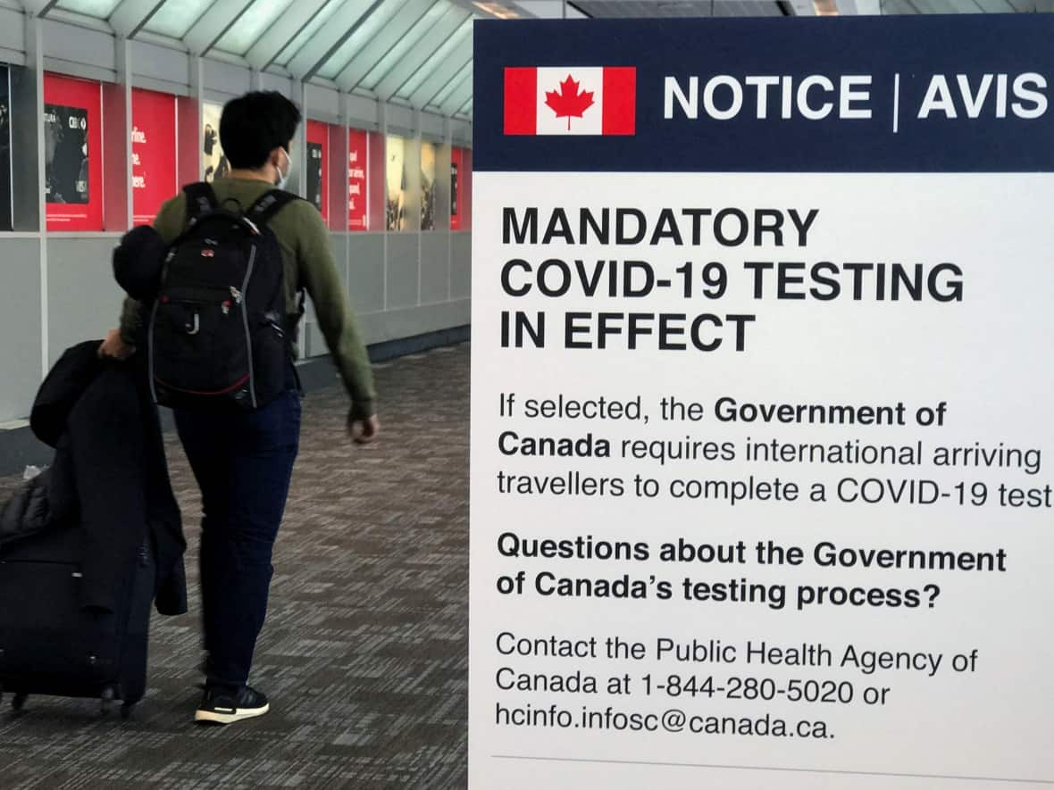 A traveller walks past a mandatory COVID-19 testing sign at Pearson International Airport in Toronto. Random testing for fully vaccinated travellers will be conducted outside of airports starting July 19. (Carlo Allegri/Reuters - image credit)