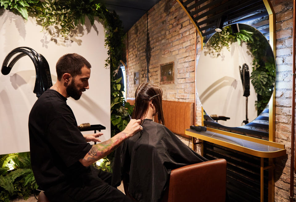 Hairstylist cutting a client's hair in a salon with green plants and mirrors