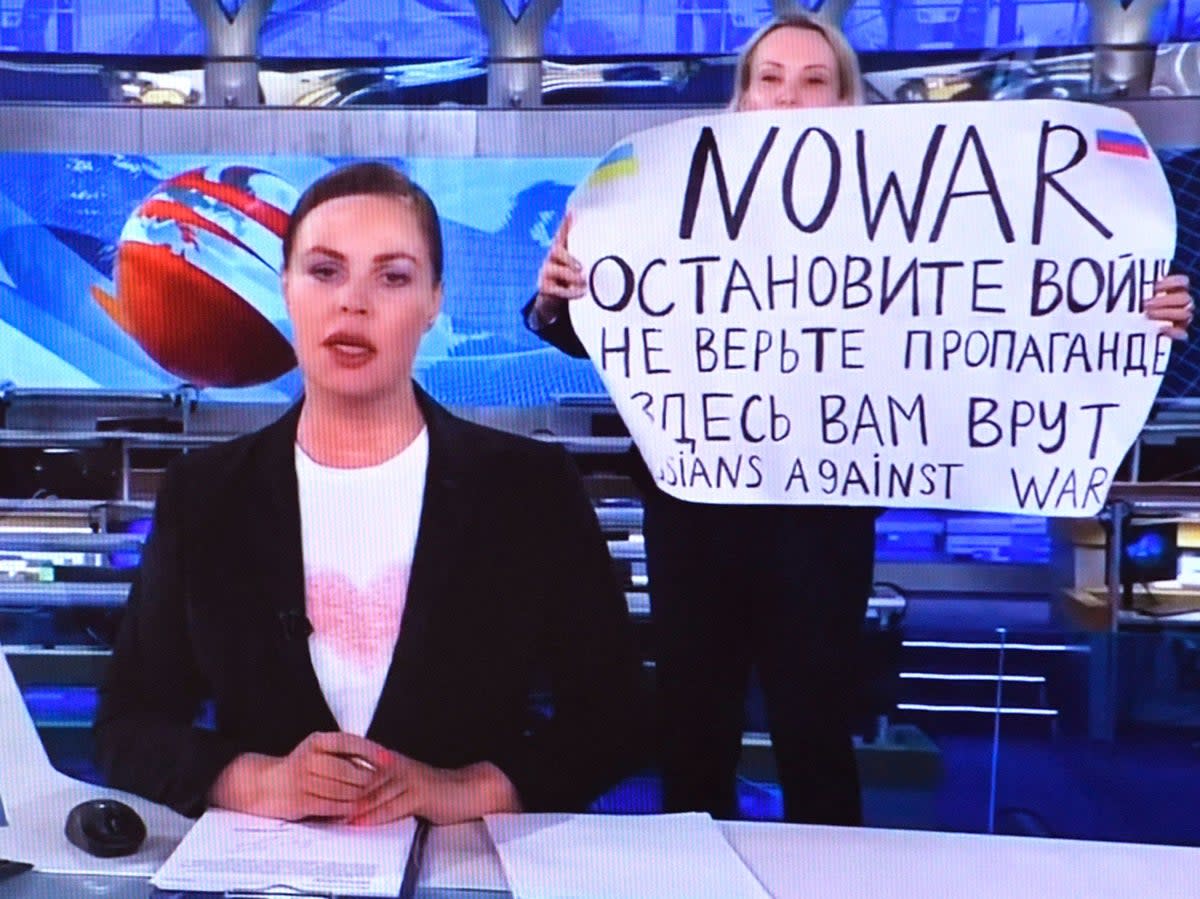 Dissenting Russian Channel One employee entering Ostankino on-air TV studio during Russia's most-watched evening news broadcast, holding up a poster which reads as 