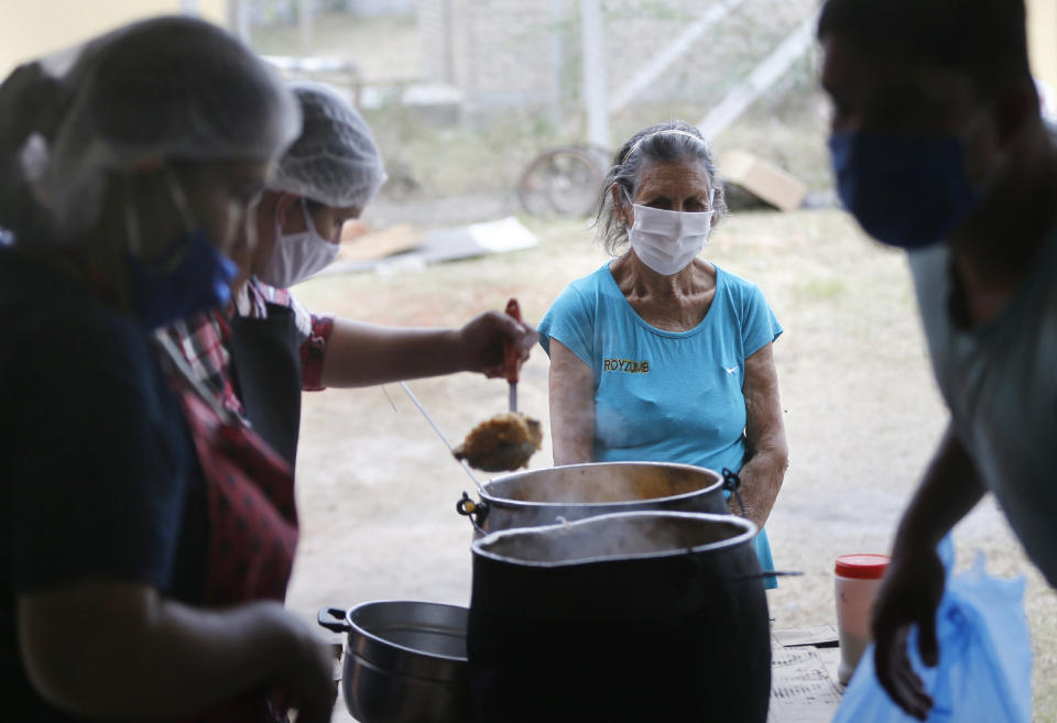 Dolores Pena waits to be served a plate of food for her and her family at a soup kitche, amid the new coronavirus pandemic, in Luque, Paraguay, Monday, May 11, 2020. Signs of mounting hunger are already being felt around the region, where desperate citizens are violating quarantines to go out in search of money and food. (AP Photo/Jorge Saenz)