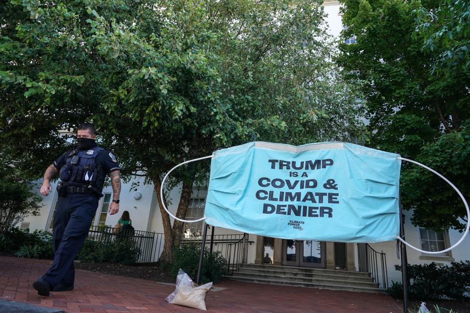 A police officer walks past a protest banner berating President Donald Trump as denying the science behind the COVID-19 pandemic and climate change set up in front of the Republican National Convention headquarters on Aug. 24 in Washington. No signs have surfaced that Trump has changed his tune. (Jemal Countess via Getty Images)