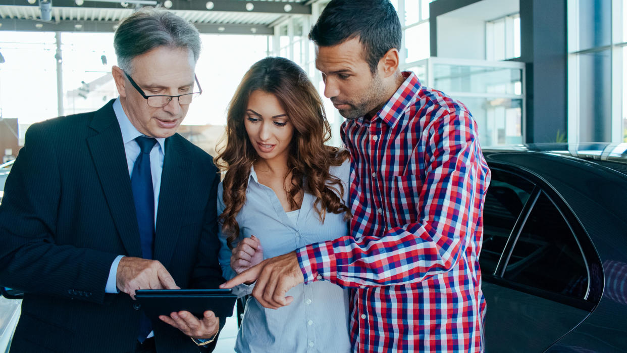 Experienced salesman selling a car to a young couple.