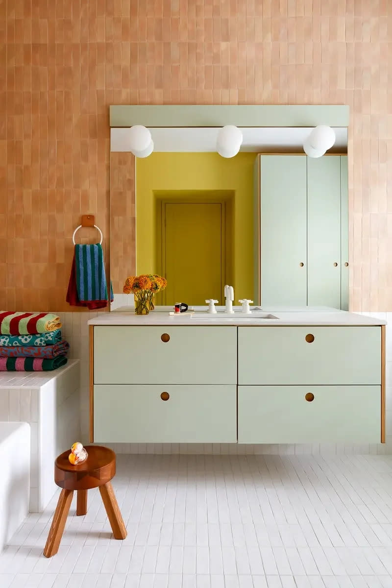 Bathroom with apricot-hued tiled wall and mint green floating vanity. 