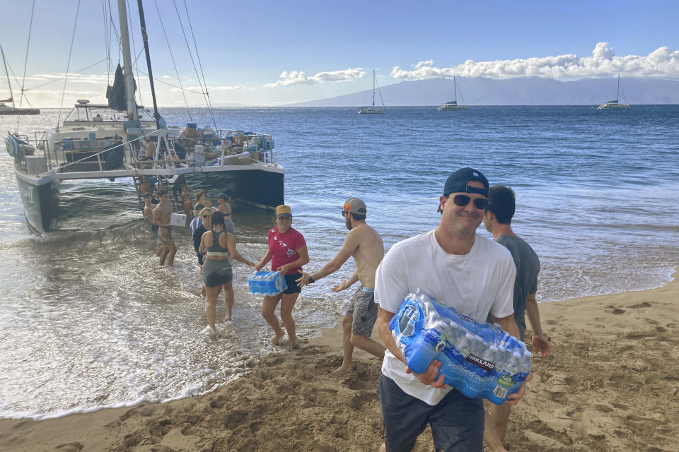 A group of volunteers who sailed from Maalaea Bay, Maui, form an assembly line on Kaanapali Beach on Saturday Aug. 12, 2023, to unload donations from a boat. Maui residents have come together to donate water, food and other essential supplies to people on the western side of the island after a deadly fire destroyed hundreds of homes and left scores of people homeless. (AP Photo/Rick Bowmer)