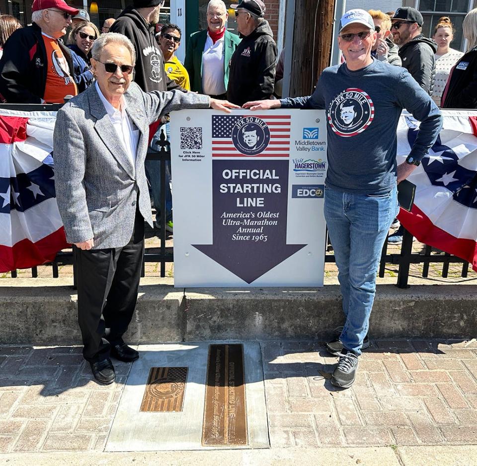 Boonsboro Mayor Howard Long, left, and JFK 50 Mile Director Mike Spinnler stand next to commemorative plaques after they were unveiled at the JFK starting line in downtown Boonsboro on March 30, 2023.