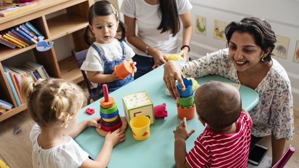 Niños pequeños jugando con la maestra en la guardería