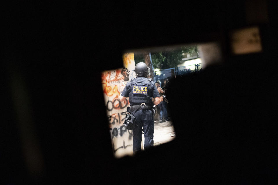 A federal officer guards the Mark O. Hatfield U.S. Courthouse as protesters gather Friday, July 24, 2020, in Portland, Ore. On the streets of Portland, a strange armed conflict unfolds night after night. It is raw, frightening and painful on both sides of an iron fence separating the protesters on the outside and federal agents guarding a courthouse inside. This weekend, journalists for The Associated Press spent the weekend both outside, with the protesters, and inside the courthouse, with the federal agents, documenting the fight that has become an unlikely centerpiece of the protest movement gripping America. (AP Photo/Noah Berger)