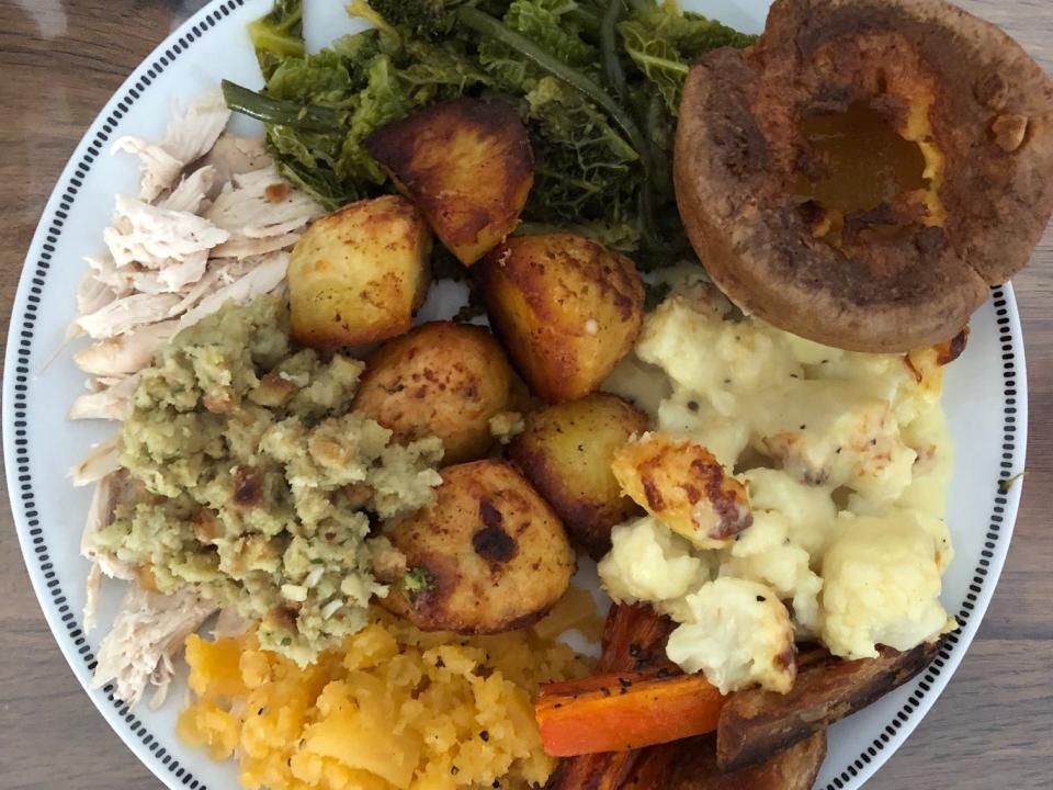 Full plate of squash, carrots, cauliflower, potatoes, stuffing, turkey, leafy greens, and a bread roll