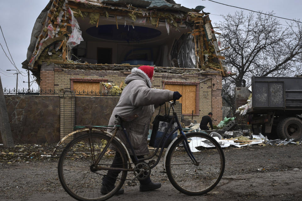 A woman passes with a bicycle as a local resident works to clean the debris from a damaged house after Russian shelling in Kramatorsk, Ukraine, Thursday, Nov. 10, 2022. (AP Photo/Andriy Andriyenko)