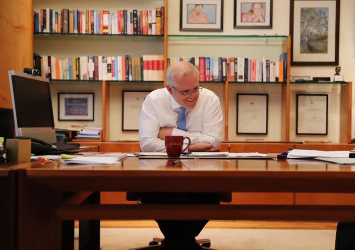 Australian Prime Minister Scott Morrison sits behind a desk smiling after a phone call with Joe Biden. 