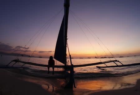 A man sits on a sailboat while waiting for tourists on a beach in Boracay, south of Manila February 2, 2008. REUTERS/Darren Whiteside/Files