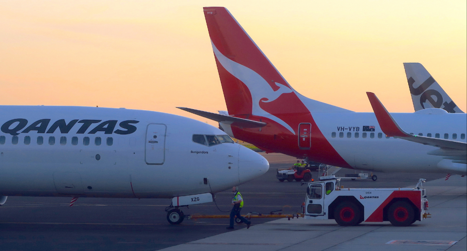 Image of Qantas planes lined up on a tarmac with a baggage handler and their truck in the foreground.