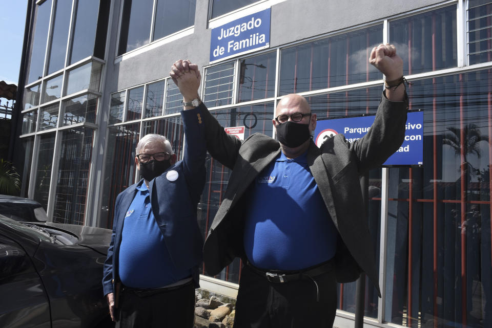 Gay equality activist Marco Castillo, left, and his longtime partner Rodrigo Campos, both wearing protective face masks, cheer in front of the cameras after they were married before a judge, in San Jose, Costa Rica, Tuesday, May 26, 2020. Costa Rica became the latest country to legalize same-sex marriage early Tuesday when a ruling from its supreme court went into effect ending the country's ban. (AP Photo/Carlos Gonzalez)