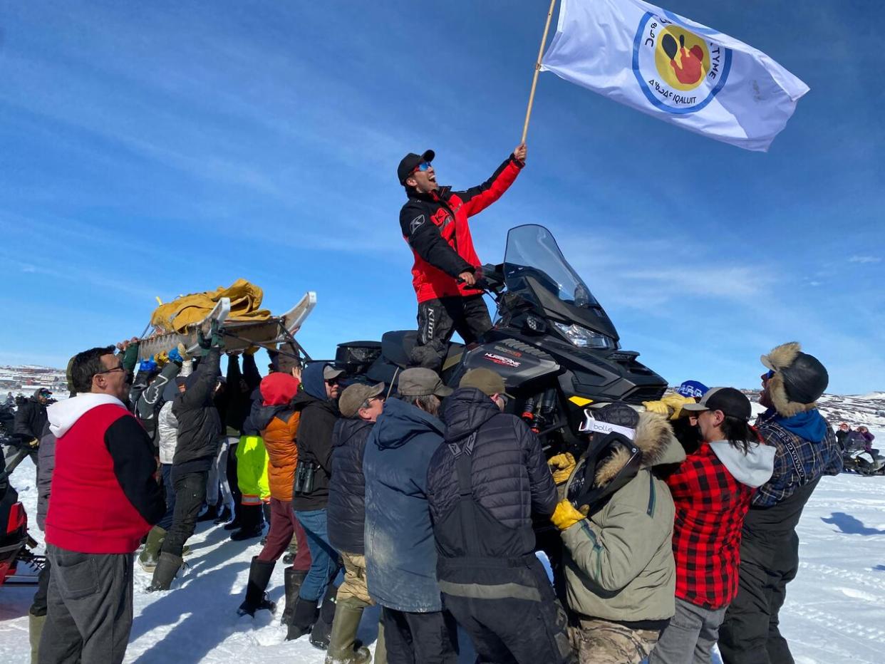 Perry Akavak, along with his snowmobile and qamutik, is lifted into the air as he celebrates winning the annual Toonik Tyme Iqaluit to Kimmirut race on Sunday.  (David Gunn/CBC  - image credit)
