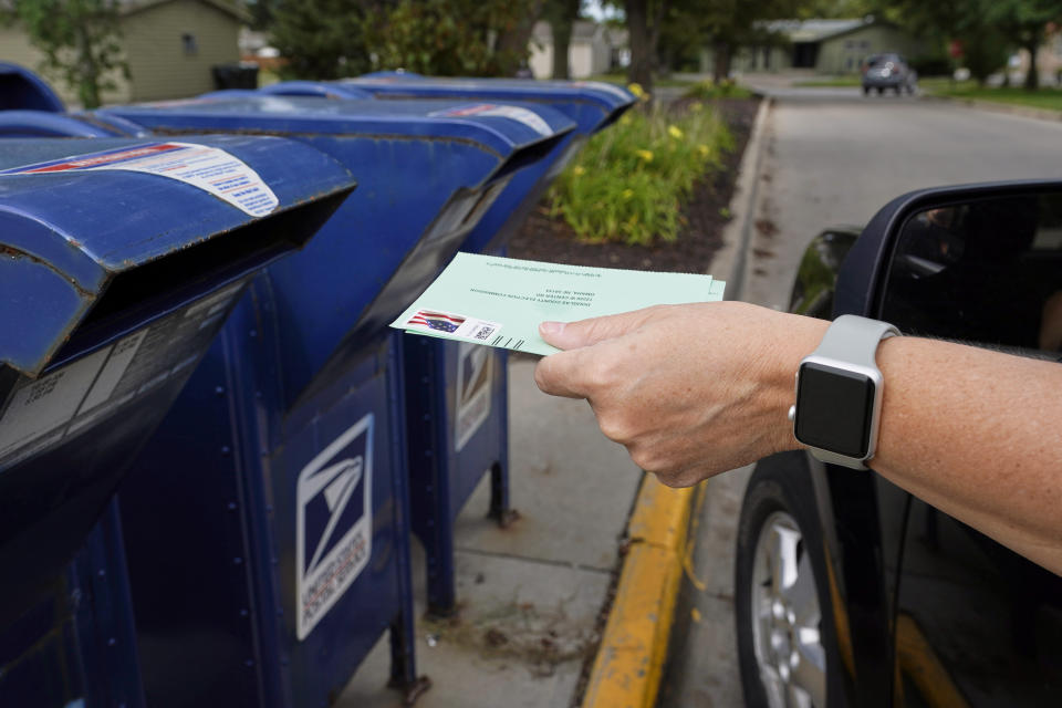 FILE - In this Tuesday, Aug. 18, 2020, file photo, a person drops applications for mail-in-ballots into a mail box in Omaha, Neb. U.S. Postal Service warnings that it can’t guarantee ballots sent by mail will arrive on time have put a spotlight on the narrow timeframes most states allow to request and return those ballots. (AP Photo/Nati Harnik, File)