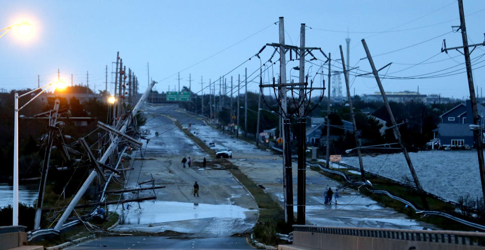 Downed power lines and a battered road is what superstorm Sandy left behind as people walk off the flooded Seaside Heights island, Tuesday, Oct. 30, 2012. Sandy, the storm that made landfall Monday, caused multiple fatalities, halted mass transit and cut power to more than 6 million homes and businesses. (AP Photo/Julio Cortez)