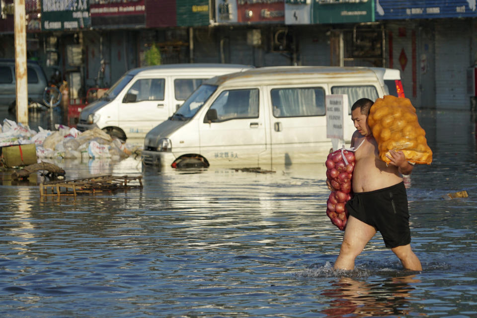 FILE - In this Monday, July 26, 2021 file photo, a man carries bags of onions out of the flooded Yubei Agricultural and Aquatic Products World in Xinxiang in central China's Henan Province. Scientists say there’s something different this year from the recent drumbeat of climate weirdness. This summer a lot of the places hit by weather disasters are not used to getting extremes and many of them are wealthier, which is different from the normal climate change victims. That includes unprecedented deadly flooding in Germany and Belgium, 116-degree heat records in Portland, Oregon and similar blistering temperatures in Canada, along with wildfires. Now Southern Europe is seeing scorching temperatures and out-of-control blazes too. And the summer of extremes is only getting started. Peak Atlantic hurricane and wildfire seasons in the United States are knocking at the door. (AP Photo/Dake Kang, File)