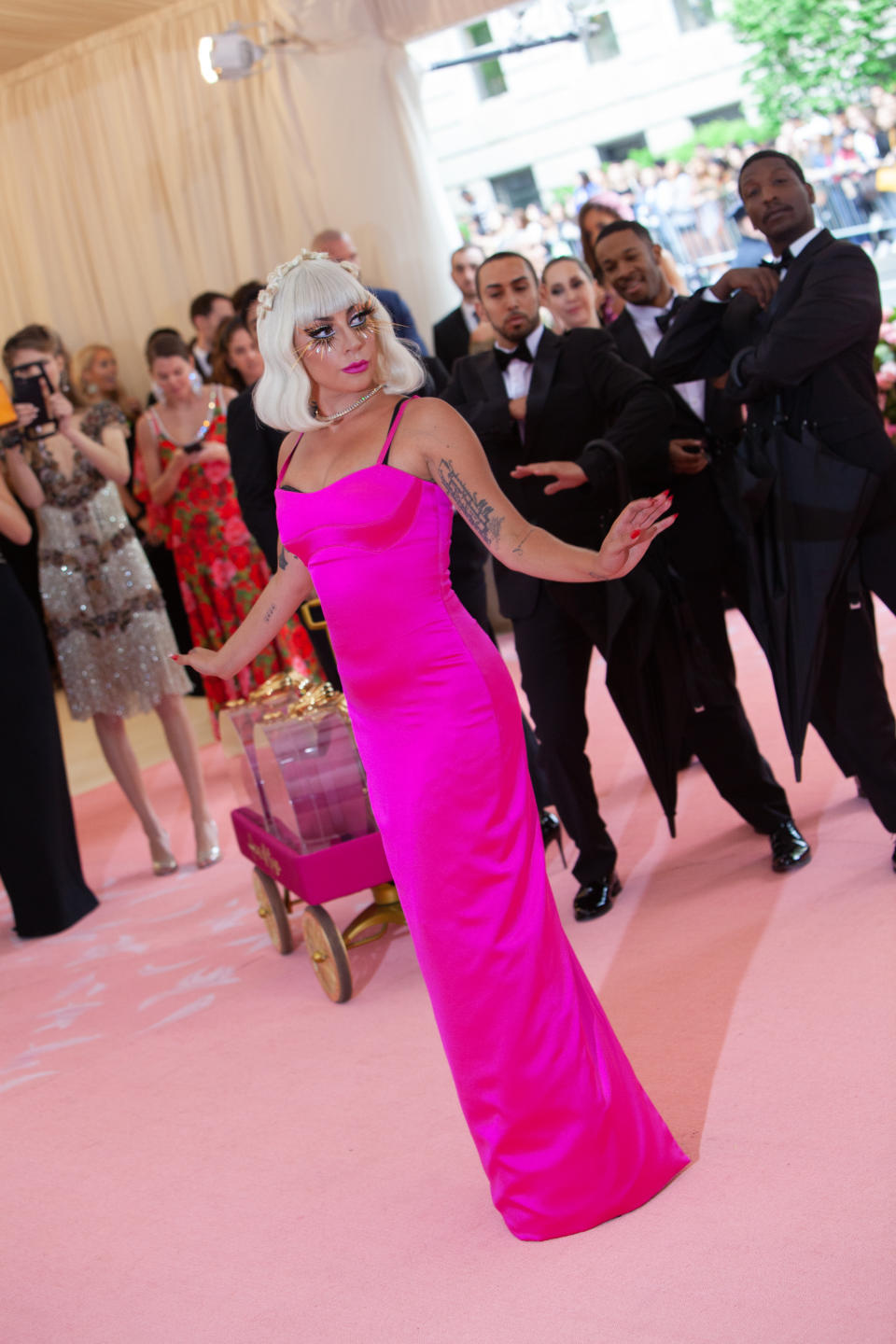 Lady Gaga is posing in a sleek gown on the red carpet, with photographers and attendees in the background capturing the moment