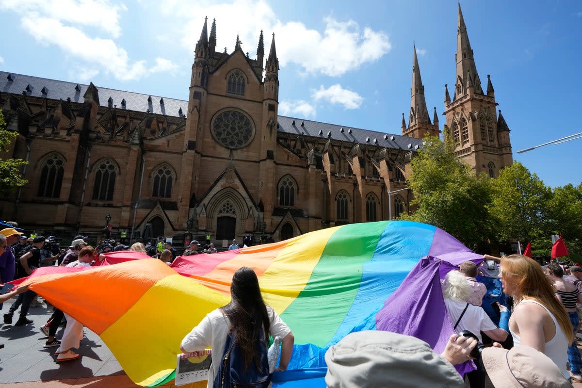 Sydney-based gay rights group Community Action for Rainbow Rights carry a large rainbow flag at George Pell’s funeral. The conservative cardinal was known to refuse Communion to those wearing rainbow-coloured sashes (AP)