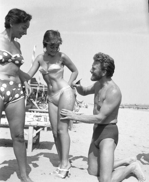 <p>Douglas autographs the thigh of painter Novella Parigini on Lido Beach in Venice. This was at the peak of his heartthrob days.</p>