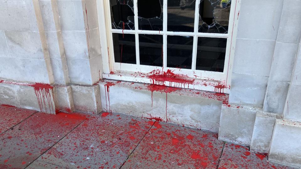 A smashed window with red paint dropping around the window frame