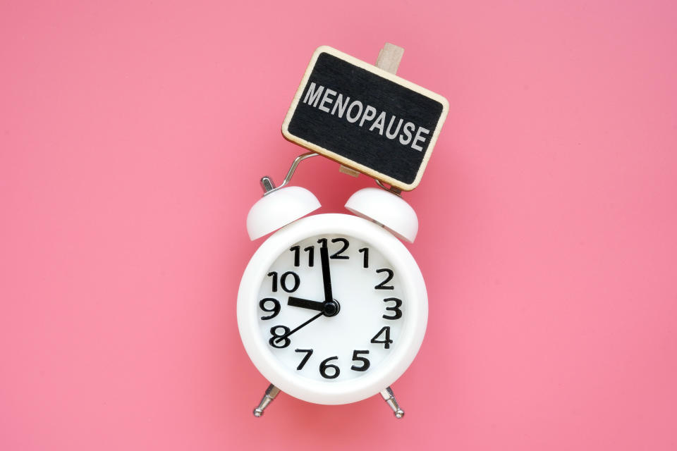 Alarm clock and word menopause on a pink background.