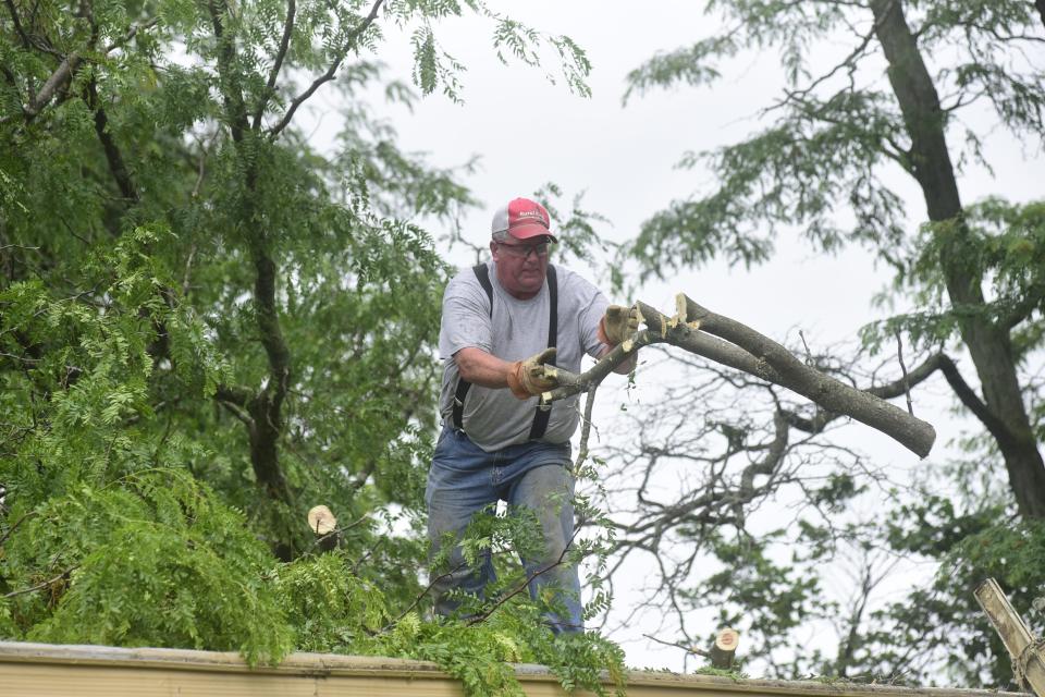 A man tosses a sawed portion of a tree limb Tuesday morning from the roof of a mobile home on Tiffin Street in Bucyrus.