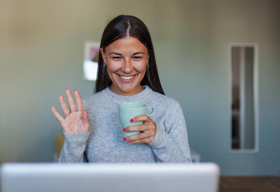 Girl waving at laptop screen and holding a mug 