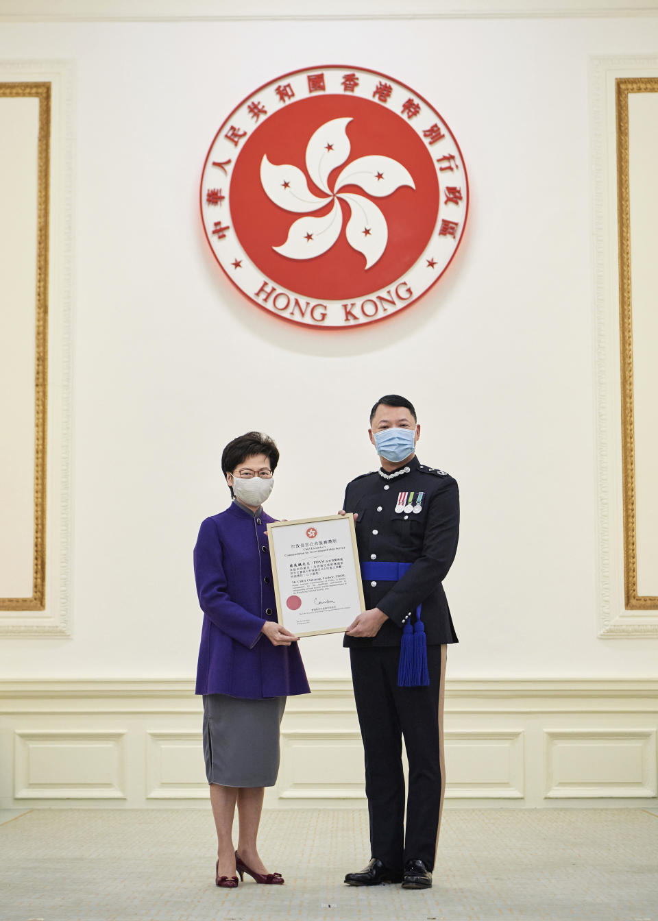 In this photo released by Hong Kong Government Information Services, Hong Kong Chief Executive Carrie Lam, left, presents the award to Hong Kong's Director of National Security Frederic Choi at Government House in recognition of his significant contributions to safeguarding national security in Hong Kong on Feb. 10, 2021. The top Hong Kong national security officer was reportedly caught up in a raid on an unlicensed massage business, and will face a police force investigation into the alleged misconduct. Choi has since been put on leave after the incident, according to Hong Kong police chief Chris Tang. (Hong Kong Government Information Services via AP)