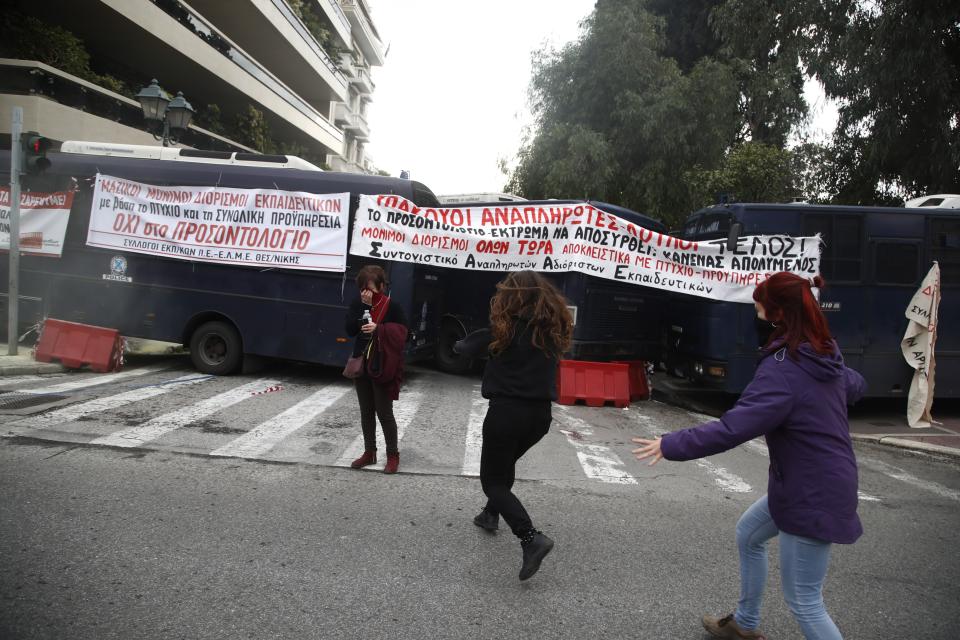 Two girls run to help a woman after riot police threw a tear gas canister during clashes near the Prime Minister's office in Athens, Friday, Jan. 11, 2019. About 1,500 people took part in the protest. Teachers' unions oppose the government's selection process for the planned hiring of 15,000 new teachers over the next three years.The banner reads ''Mass Full Time Hiring for Teachers.'' (AP Photo/Thanassis Stavrakis)