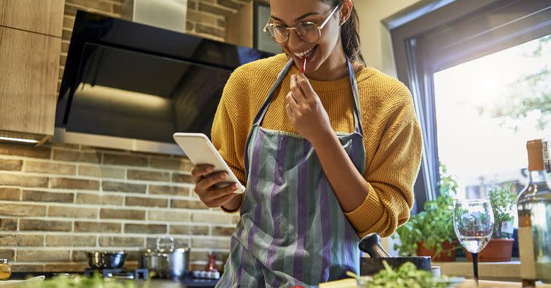 young woman consulting smartphone for recipe while cooking in kitchen