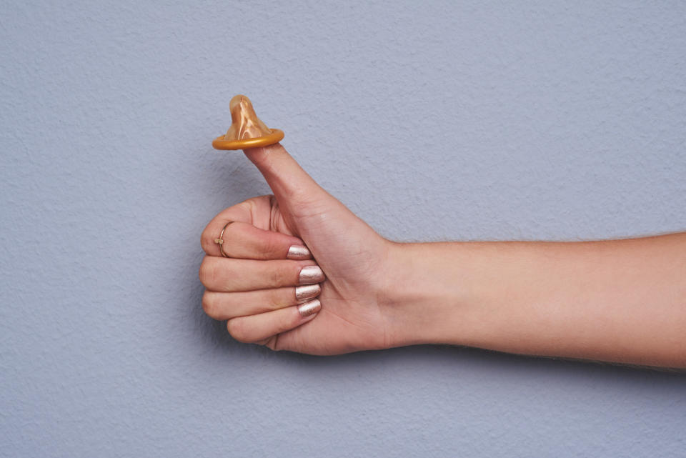 a person's hand in a thumbs-up position with the top of a condom on the thumb