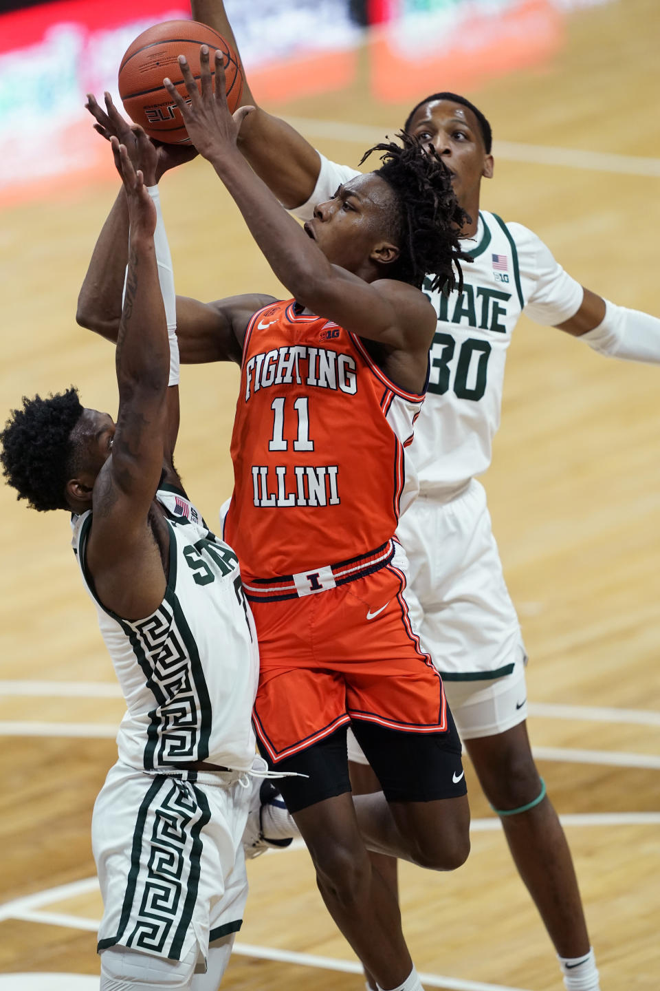 Illinois guard Ayo Dosunmu (11) shoots over the defense of Michigan State guard Rocket Watts (2) and forward Marcus Bingham Jr. (30) during the first half of an NCAA college basketball game, Tuesday, Feb. 23, 2021, in East Lansing, Mich. (AP Photo/Carlos Osorio)