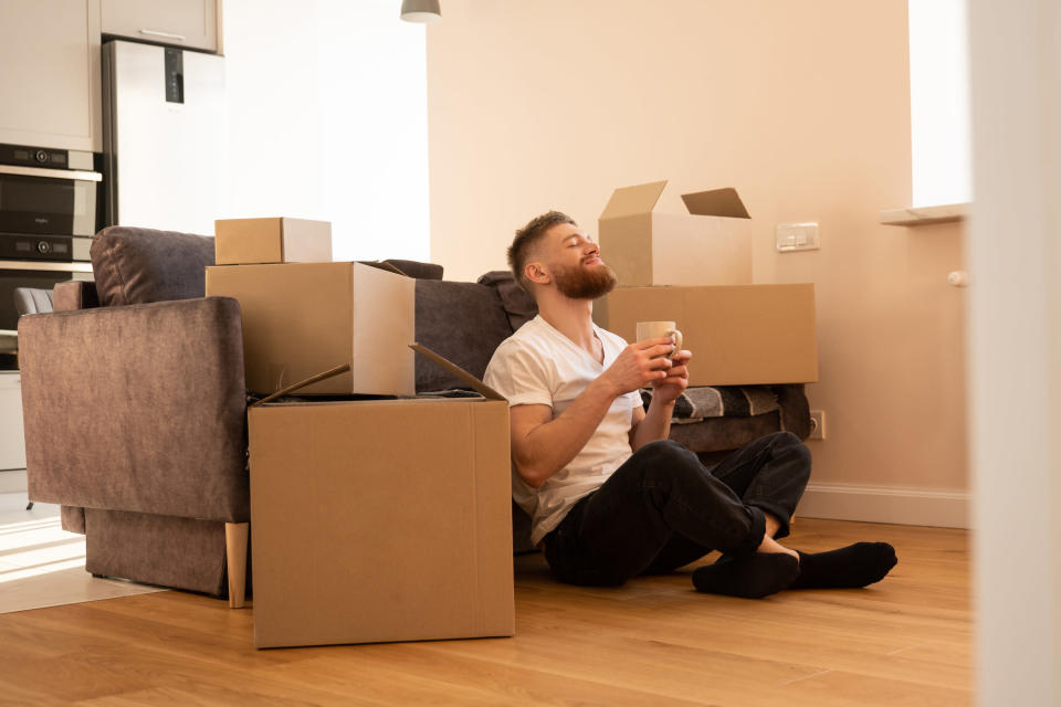 Man with a coffee sits near boxes in his studio apartment