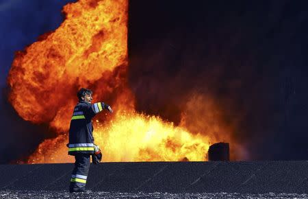 A firefighter stands near the fire of a storage oil tank at the port of Es Sider in Ras Lanuf December 29, 2014. REUTERS/Stringer