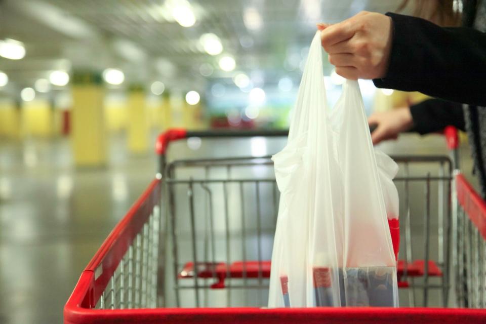 A plastic bag full of groceries being placed in a shopping cart. 