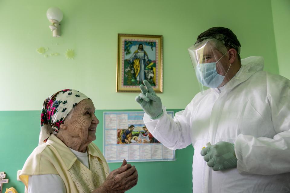 In this photo taken on Thursday, May 28, 2020, Father Yaroslav Rokhman, a priest of Ukrainian Greek Catholic Church wearing a special suit and visor to protect against coronavirus blesses a patient of the hospice in Ivano-Frankivsk, Ukraine. Rokhman, a priest in the Ukrainian Greek Catholic Church, is pleased to be able to return to performing one of a cleric's most heartfelt duties. As the coronavirus pandemic's grip on Ukraine slowly recedes, priests received permission on May 22 to again hold services and visit the sick. (AP Photo/Evgeniy Maloletka)