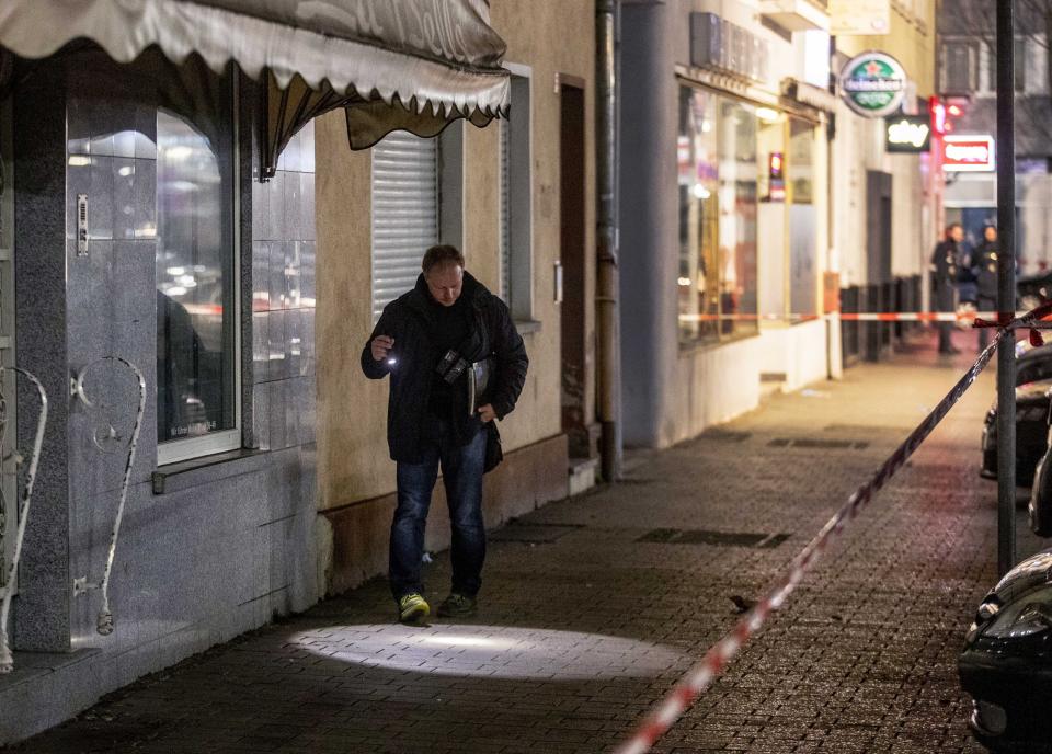 A police officer looks for evidence in front of a restaurant at the scene of a shooting in central Hanau, Germany Thursday, Feb. 20, 2020. Eight people were killed in shootings in the German city of Hanau on Wednesday evening, authorities said. Two hookah lounges reportedly were targeted. (AP Photo/Michael Probst)