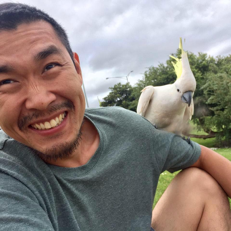 Yun-Seob Shin smiles with a cockatoo perched on his shoulder. 