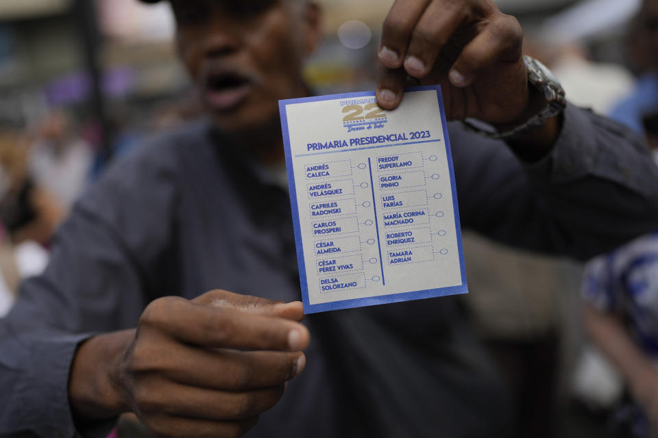 Un hombre explica cómo votar mientras sostiene una boleta sin marcar mientras abre un colegio electoral para las elecciones primarias presidenciales de la oposición en la plaza Luis Brión en Caracas, Venezuela, el domingo 22 de octubre de 2023. La oposición elegirá un candidato para desafiar al presidente Nicolás Maduro en las elecciones presidenciales de 2024. (Foto AP/Matías Delacroix)