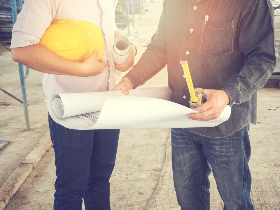 Two people looking at blueprints at a construction site.