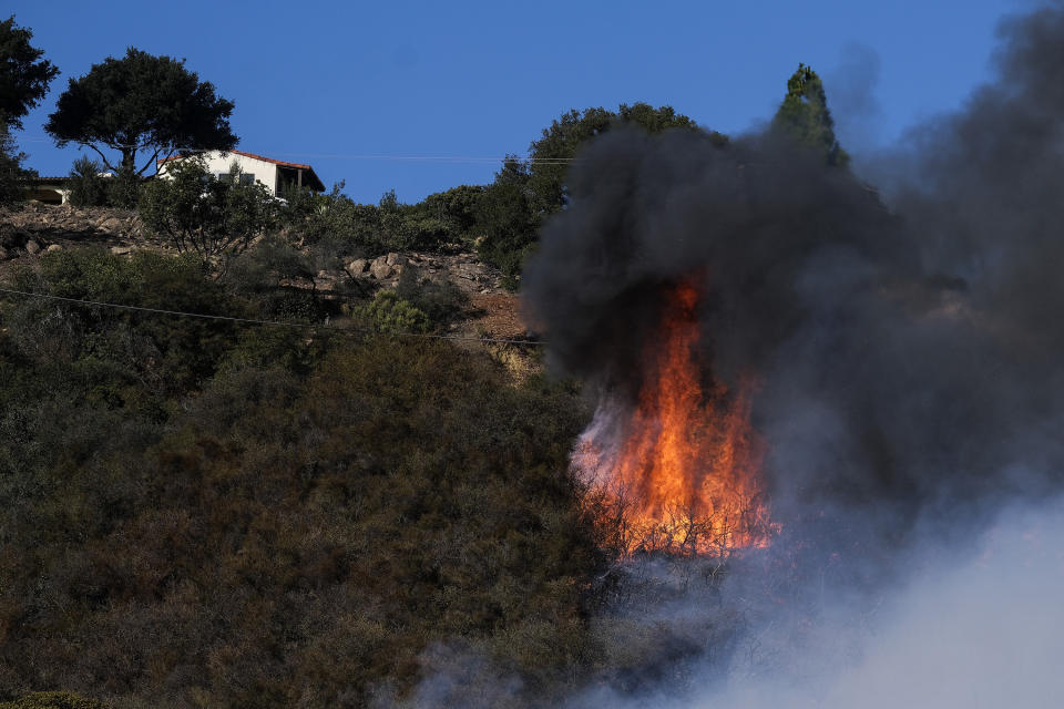 A wildfire burns near a home Wednesday, Oct. 13, 2021, in Goleta, Calif. A wildfire raging through Southern California coastal mountains threatened ranches and rural homes and kept a major highway shut down Wednesday as the fire-scarred state faced a new round of dry winds that raise risk of flames. The Alisal Fire covered more than 22 square miles (57 square kilometers) in the Santa Ynez Mountains west of Santa Barbara. (AP Photo/Ringo H.W. Chiu)